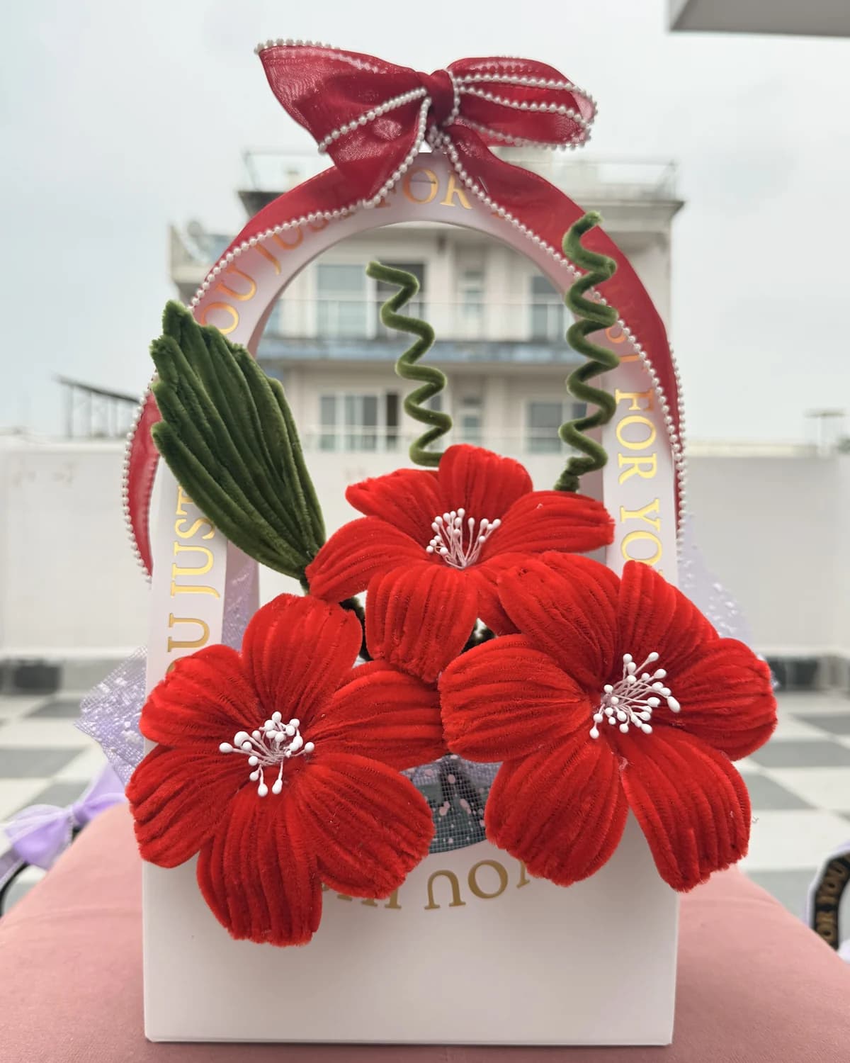 handmade chenille flowers standing in an arched "just for you" carrier bag tied with an organza bow — red blooms