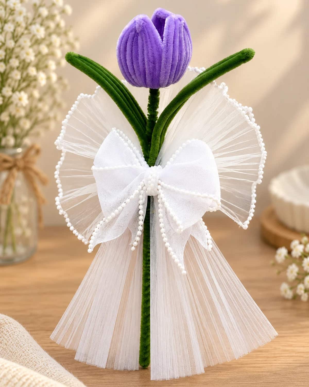 single handmade tulip on a green stem, wrapped in white pleated organza with a pearl-edged bow